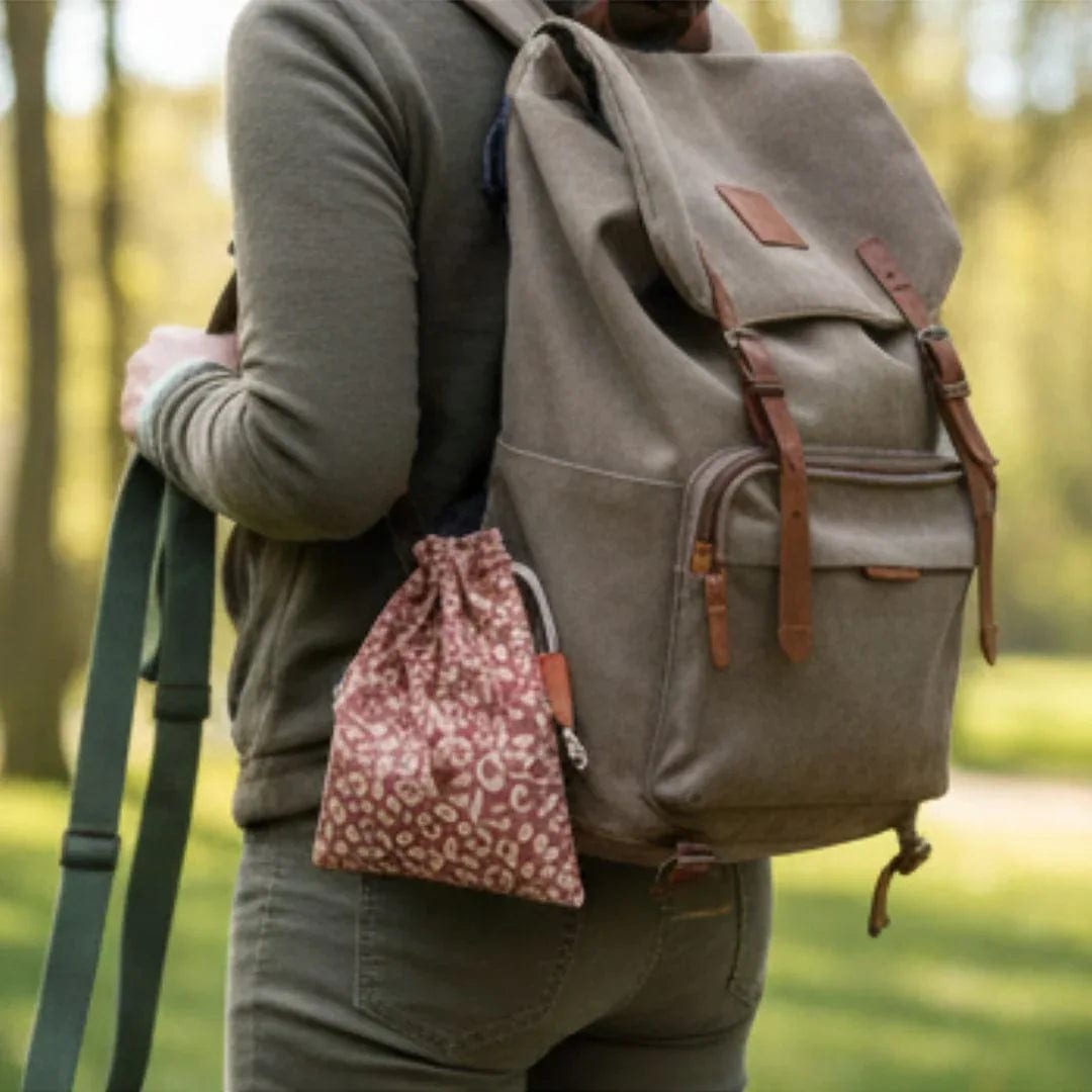 Person trägt grauen Rucksack mit hellbraunen Lederdetails. An einer Seite hängt ein kleiner, beiger Beutel mit pinkem Blütenmuster. Outdoor
