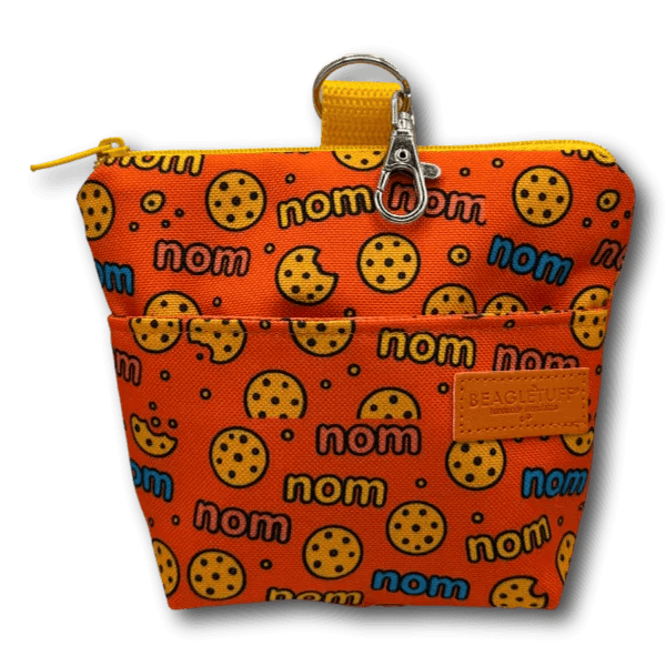 Orangener LeckerliBeutel mit Muster aus Keksen und dem Schriftzug "nom" in Blau, Gelb und Pink, mit Reißverschluss oben und Karabinerhaken,