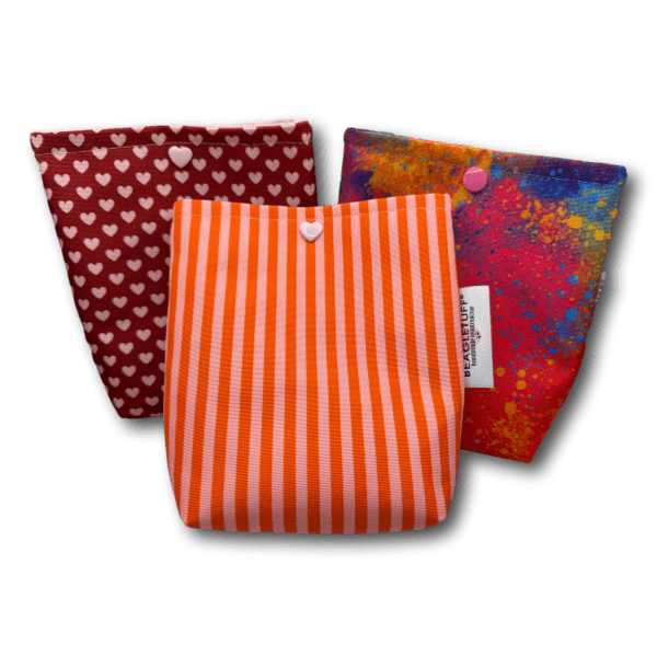 Drei farbige kleine Taschen aus robustem Stoff mit unterschiedlichen Mustern: rot mit weißen Herzen, orange mit weißen Streifen und bunt ges