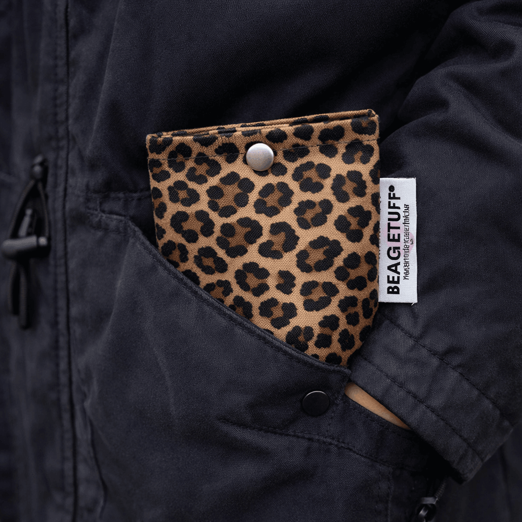Leopardgemusterte, braun-schwarze kleine Tasche mit Druckknopf, teilweise in dunkler Jackentasche steckend, an der Taschenseite ein weißes B